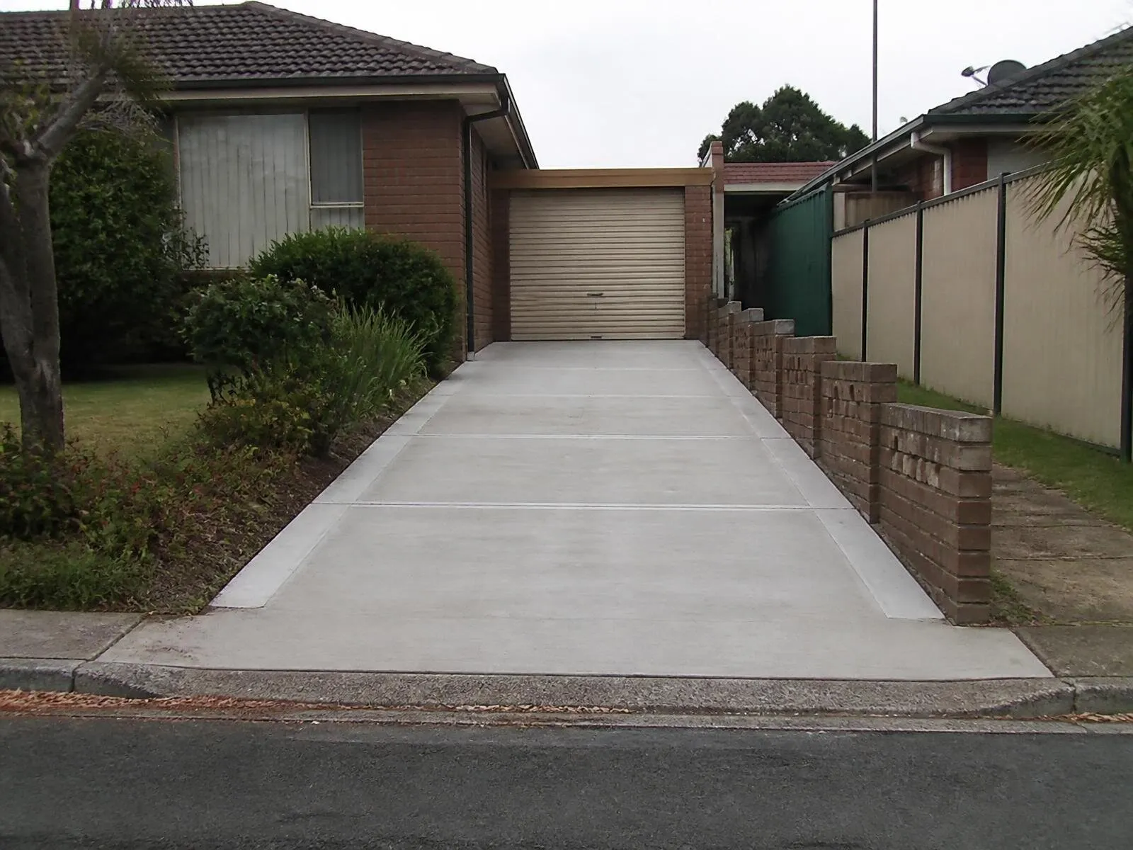 The same concrete driveway from the same camera position after pressure cleaning, with the staining removed