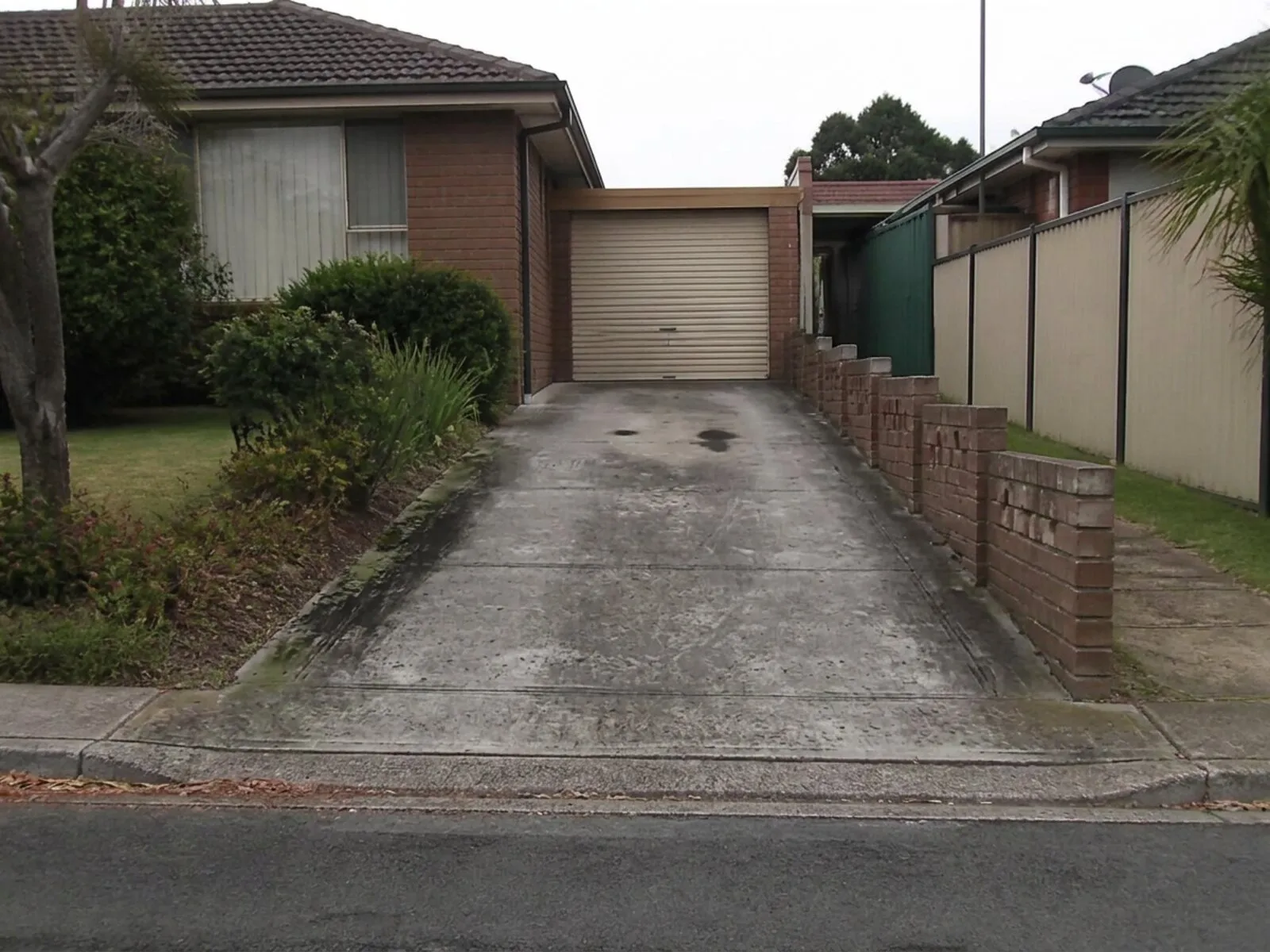 Concrete driveway of a suburban brick home stained with mould streaks and traffic grime before pressure cleaning